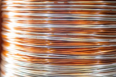 Üst üste yığılmış metalik tel bobinlerin yakın çekim görüntüleri karmaşık desenlerini ve yansıtıcı yüzeylerini gösteriyor. Görüntü, sıkıca sarılmış tellerdeki ışık ve gölgenin etkileşimini yakalıyor. Endüstriyel maddedeki ustalığı ve hassasiyeti vurguluyor.