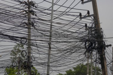 Bangkok, Tayland 'daki elektrik direğine bağlı sayısız kablo ve kablodan oluşan kaotik bir karmaşa. Karmaşık iletişim ve elektrik hatları, gri gökyüzüne ve bulanık yeşilliğe karşı görsel olarak ezici bir sahne yaratıyor..