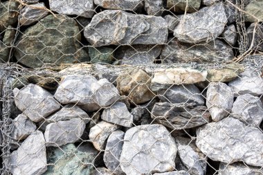 Gabion duvar, gri taşların ve tel örgülerin dokusunu gösteriyor. Görüntü, inşaat malzemesinin ayrıntılı yapısını ve dayanıklı yapısını vurguluyor..