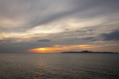 Güneş ufkun altına batıyor, sakin denizin üzerine altın bir parıltı saçıyor. Yalnız bir yelkenli körfez boyunca huzur içinde süzülürken hafif bir esinti suyu dalgalandırır. Martılar tepeden ağlar, sakin atmosferi artırır..