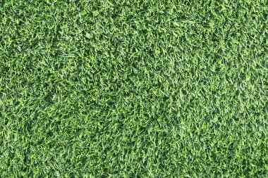 yemyeşil suni bir çimenliğe yakın çekim. Çimenlerin sentetik yaprakları mükemmel bir şekilde hizalanmış ve halı benzeri bir arka plan oluşturuyor.