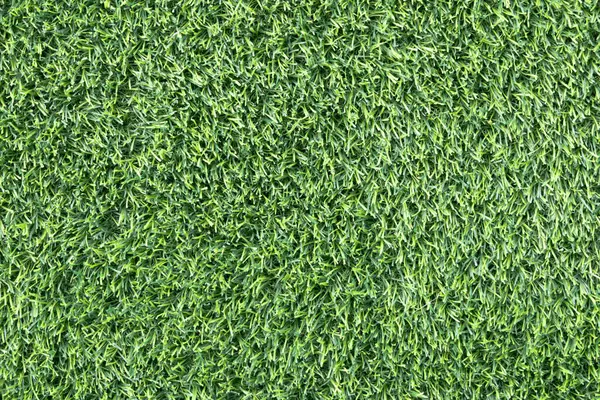 yemyeşil suni bir çimenliğe yakın çekim. Çimenlerin sentetik yaprakları mükemmel bir şekilde hizalanmış ve halı benzeri bir arka plan oluşturuyor.