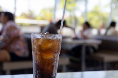 Bir bardak buz gibi kola masanın üzerinde duruyor, yoğunlaşma camda parlıyor. Köpükler davetkar bir şekilde köpürüyor, ferahlatıcı bir içecek vaat ediyor..