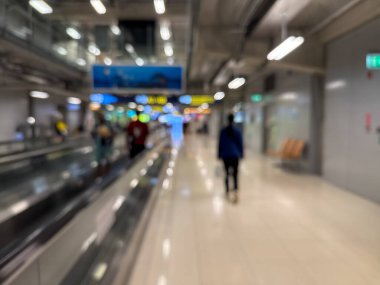 Havaalanı terminali boyunca yürüyen bir yürüyüş yolu ve modern mimari detaylarla yürüyen gezginlerin bulanık görüntüsü.