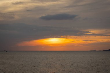 Güneş ufkun altına batıyor, sakin denizin üzerine altın bir parıltı saçıyor. Yalnız bir yelkenli körfez boyunca huzur içinde süzülürken hafif bir esinti suyu dalgalandırır. Martılar tepeden ağlar, sakin atmosferi artırır..