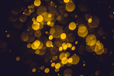 Koyu bir arka planda farklı boyut ve renklerde odanmamış altın bokeh ışıkları.