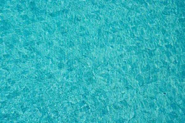 Parıldayan yansımaları ve güneş ışığı altında dalgalanmaları olan canlı mavi su yüzeyi.