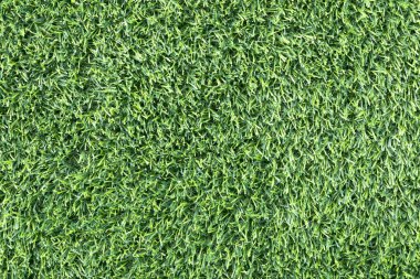 yemyeşil suni bir çimenliğe yakın çekim. Çimenlerin sentetik yaprakları mükemmel bir şekilde hizalanmış ve halı benzeri bir arka plan oluşturuyor.