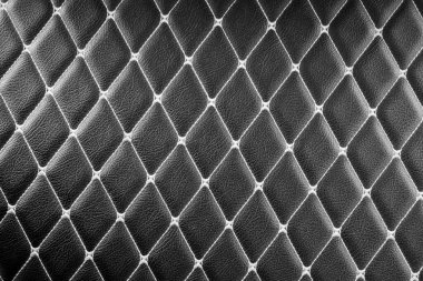 Elmas şekilli dikişli siyah deri bir yüzeye yakın plan. Derinin derin, zengin rengi ve karmaşık dikişler lüks ve sofistike bir görünüm yaratıyor.