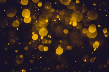 Koyu bir arka planda farklı boyut ve renklerde odanmamış altın bokeh ışıkları.