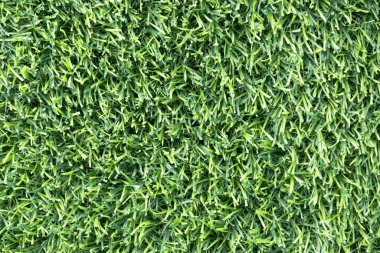 yemyeşil suni bir çimenliğe yakın çekim. Çimenlerin sentetik yaprakları mükemmel bir şekilde hizalanmış ve halı benzeri bir arka plan oluşturuyor.