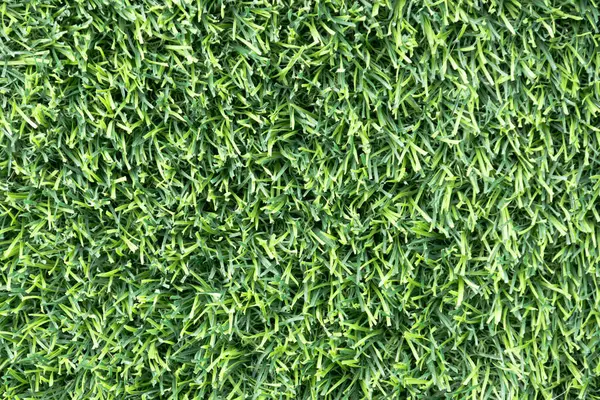 yemyeşil suni bir çimenliğe yakın çekim. Çimenlerin sentetik yaprakları mükemmel bir şekilde hizalanmış ve halı benzeri bir arka plan oluşturuyor.