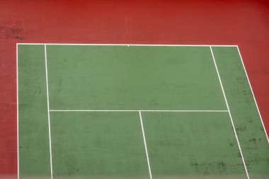 Canlı kırmızı ve yeşil açık hava tenis kortunun beyaz çizgileri, spor, dinlenme ve kentsel manzara temaları için ideal bir görüntüsü.