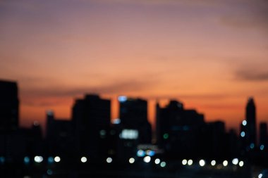 Bulanık binalar ve parlak turuncu ve pembe günbatımı gökyüzüne vuran Bokeh ışıkları. Görüntü sakin ve kentsel bir ortam yaratıyor..