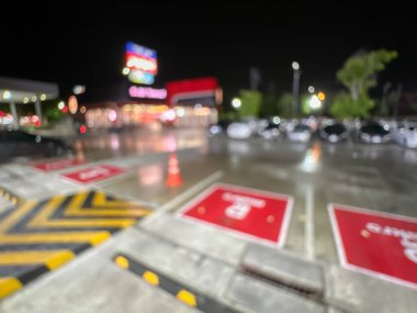 Geceleri bir marketin park alanının bulanık görüntüsü, parlak ışıklı park alanları ve aydınlatılmış mağaza tabelaları.