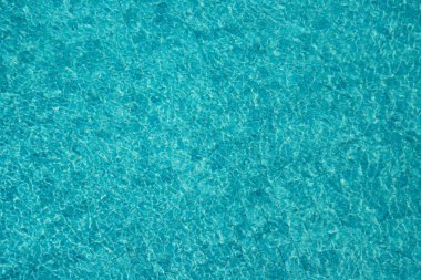 Parıldayan yansımaları ve güneş ışığı altında dalgalanmaları olan canlı mavi su yüzeyi.