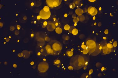 Koyu bir arka planda farklı boyut ve renklerde odanmamış altın bokeh ışıkları.