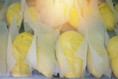 Beyaz kağıda sarılmış taze durian meyveleri, sarı rengini vurgulayan sıcak ışıklarla bir pazarda sergileniyor.