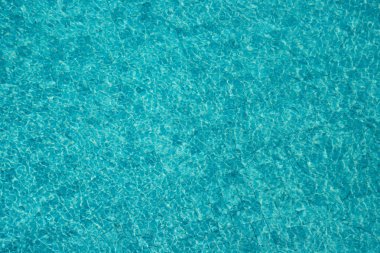 Parıldayan yansımaları ve güneş ışığı altında dalgalanmaları olan canlı mavi su yüzeyi.