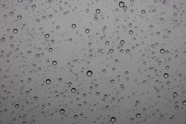 Yayılmış ışık tarafından aydınlatılan cam bir yüzeye tutunarak çeşitli boyutlarda su damlacıklarının yakın çekim, tam kare görüntüsü..