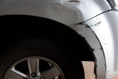 Gümüş bir arabanın ön çamurluğunda ve tamponunda hasar var. Görünürde göçükler, çizikler ve boya hasarı var. Çarpışma ya da darbeyi işaret ediyor. Görüntü otomatik kaporta onarımına duyulan ihtiyacı vurgular.