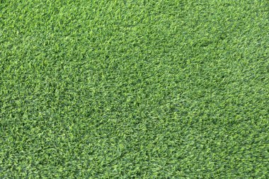 yemyeşil suni bir çimenliğe yakın çekim. Çimenlerin sentetik yaprakları mükemmel bir şekilde hizalanmış ve halı benzeri bir arka plan oluşturuyor.