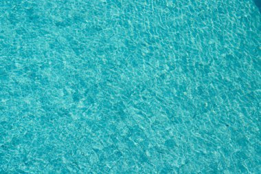 Parıldayan yansımaları ve güneş ışığı altında dalgalanmaları olan canlı mavi su yüzeyi.