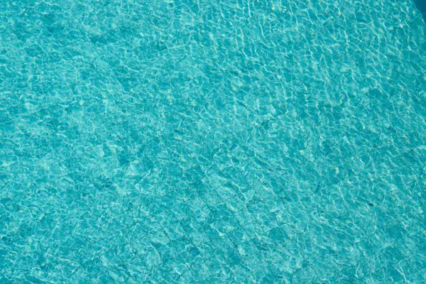 Parıldayan yansımaları ve güneş ışığı altında dalgalanmaları olan canlı mavi su yüzeyi.