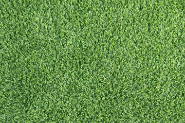 yemyeşil suni bir çimenliğe yakın çekim. Çimenlerin sentetik yaprakları mükemmel bir şekilde hizalanmış ve halı benzeri bir arka plan oluşturuyor.