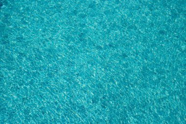 Parıldayan yansımaları ve güneş ışığı altında dalgalanmaları olan canlı mavi su yüzeyi.