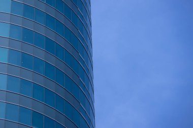 Modern bir binanın birçok dikdörtgen pencereli bir bölümü berrak, parlak mavi gökyüzünü yansıtıyor..