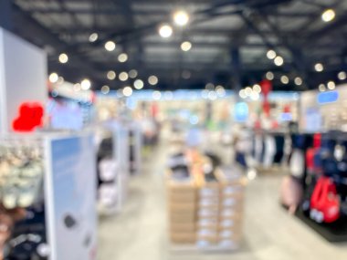 Bir alışveriş merkezinin içini gösteren bulanık bir görüntü. Olay yeri bulanık, belirsiz dükkanlar, ışıklar ve yürüyen insanlarla dolu. Genel izlenim yumuşak ve soyut.