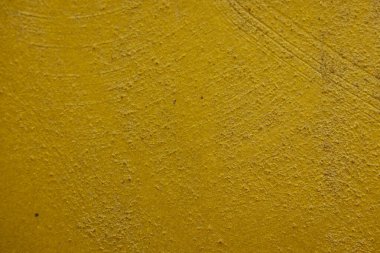 Kalıplı sarı beton yüzeyin yakın plan çekimi. Kaba ve biraz pürüzlü doku ve altın sarısındaki ince varyasyonlar, görsel olarak ilginç bir zemin oluşturur. Bazı ince yatay çizgiler görünür..