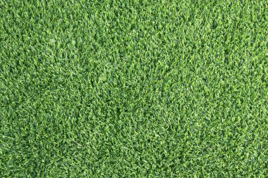 yemyeşil suni bir çimenliğe yakın çekim. Çimenlerin sentetik yaprakları mükemmel bir şekilde hizalanmış ve halı benzeri bir arka plan oluşturuyor.