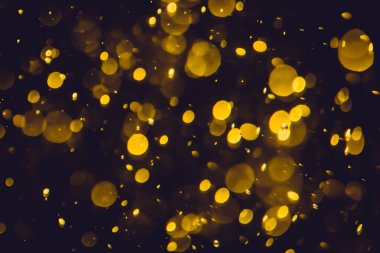 Koyu bir arka planda farklı boyut ve renklerde odanmamış altın bokeh ışıkları.