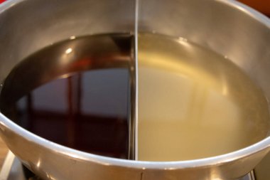 Metal bir güveç tenceresi iki bölüme ayrılır, biri koyu kahverengi bir çorba, diğeri ise açık renkli, açık renkli bir çorba ile..