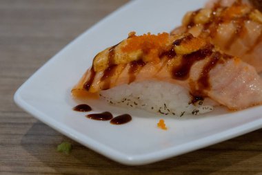 Beyaz bir tabakta kurutulmuş somon nigiri suşisi, yumurta ve sos serpiştirilmiş..