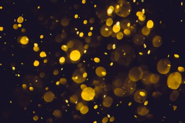 Koyu bir arka planda farklı boyut ve renklerde odanmamış altın bokeh ışıkları.
