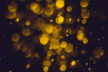 Koyu bir arka planda farklı boyut ve renklerde odanmamış altın bokeh ışıkları.