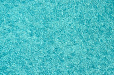 Parıldayan yansımaları ve güneş ışığı altında dalgalanmaları olan canlı mavi su yüzeyi.