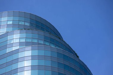 Modern bir binanın birçok dikdörtgen pencereli bir bölümü berrak, parlak mavi gökyüzünü yansıtıyor..