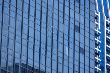 Modern bir binanın birçok dikdörtgen pencereli bir bölümü berrak, parlak mavi gökyüzünü yansıtıyor..