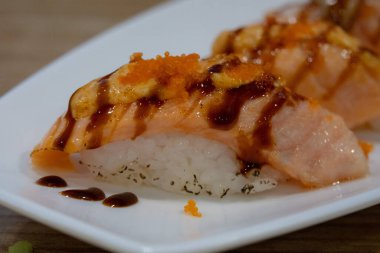 Beyaz bir tabakta kurutulmuş somon nigiri suşisi, yumurta ve sos serpiştirilmiş..