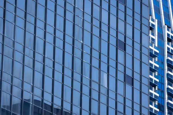 Modern bir binanın birçok dikdörtgen pencereli bir bölümü berrak, parlak mavi gökyüzünü yansıtıyor..