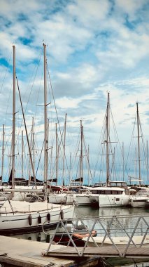 Rıhtıma yanaşmış yelkenli ve yatlarla dolu pitoresk bir marina, mavi, bulutlu bir gökyüzünün zeminine kurulmuş..