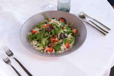 Beyaz masa örtüsünde servis edilen domatesli, zeytinli ve peynirli taze yeşil salata sağlıklı bir yemek için idealdir..
