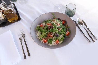 Zeytin, domates ve peynirli, zeytinyağı ve baharatlarla birlikte beyaz masa örtüsünde servis edilen taze bir salata..