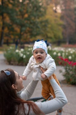 Genç anne dışarıda parkta neşeli bir bebeği kucağına alıyor.