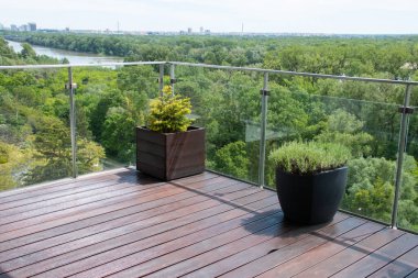 Bir balkon, biri yeşil yapraklı iki büyük saksı bitkisine ve diğeri de yayılan yeşil ağaçların panoramik görünümüne karşı kokulu bir bitkiye sahiptir..