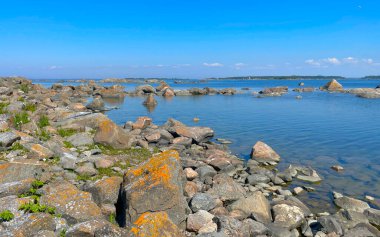 Parlak mavi gökyüzünün altında güzel kayalar ve kristal berrak suların yer aldığı sakin ve sakin bir sahil manzarası.